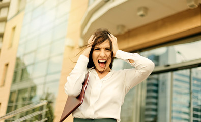 Young hysterical business woman screaming and holding her head her arms against the background of a business center