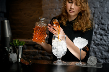 female bartender pours drink from jigger into cup.
