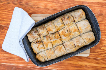 Apple pie homemade strudel in a baking iron plate on a wooden table just out of the oven. Pie with apples, raisins and cinnamon, sweet pastries