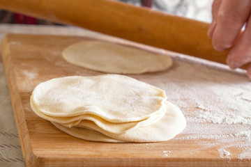 Rolled dough cakes on a board with flour on a wooden rolling pin background. Close-up
