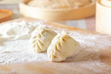 Raw manti, dumplings or wonton from dough with minced meat filling on the kitchen table with flour on a background of a wooden double boiler. Homemade food. Close-up.