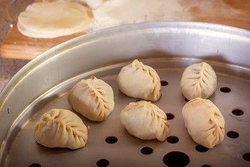 Raw manti, dumplings or wonton from dough with minced meat filling are placed in a double boiler on the background of the kitchen table. Homemade food. Close-up.