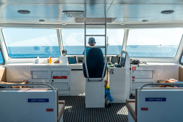 Boat captain driving ship in ocean water, with engine, throttle, controls. Sailing ship in open water.