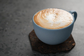Fresh cappuccino in blue cup on concrete background