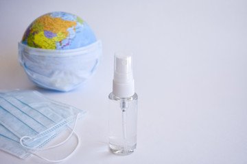 A standard face mask on a globe model. Corona virus concept. Medical face mask for stopping the spread of flu virus. Bottle with an antiseptic for cleansing hands. Covid-19. Blurred background.