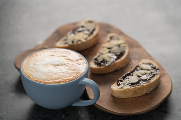 Fresh cappuccino in blue cup with toasts with chocolate spread on concrete background