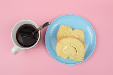 Slice of Swiss roll cake with cup of coffee on Pink Background.