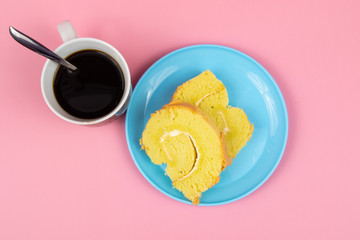 Slice of Swiss roll cake with cup of coffee on Pink Background.
