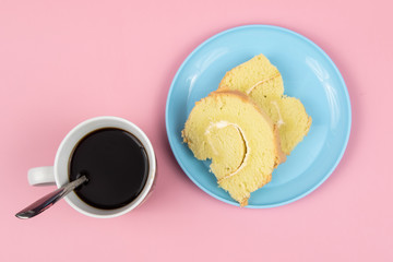 Slice of Swiss roll cake with cup of coffee on Pink Background.