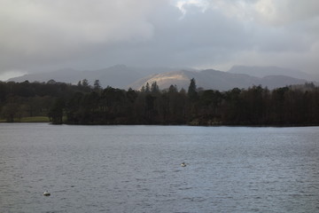 Lake with a forest and a mountain in the background and clouds on the sky  with light in between