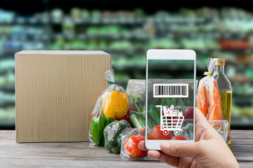 Online order grocery shopping on touch screen concept. Hand holding smart phone with checks the bar code on packaging fresh vegetable on label for ingredient and payment. Business with technology.