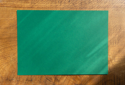 Design template in the form of a green sheet of paper on a textured gold oak wooden surface with place for text or copy space for banners, advertising, print. Atmospheric mockup for lettering.