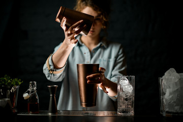 young girl at bar pours drink from one metal cup to another