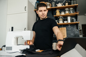 attractive male seamstress uses a tablet and watches video tutorials on manufacturing clothes. Remote work.