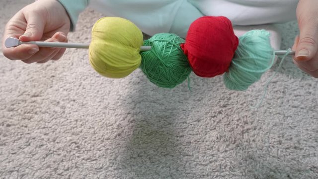 Hands demonstrate four balls of different colours on metal knitting needle. Close up
