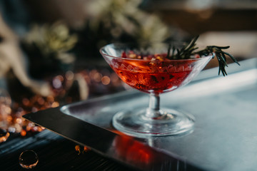 a glass with a cocktail of red color with rosemary on a dark background