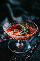 a glass with a cocktail of red color with rosemary on a dark background