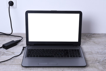 Laptop, computer is charging from a 220-volt outlet on a desk near the wall. Energy, accumulation. Mockup