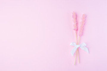 Rock candy on pink paper background decorated with a white bow, horizontal, top view, copy space