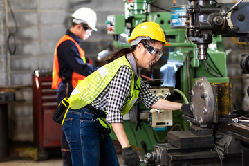 Woman worker wearing safety goggles control lathe machine to drill components. Metal lathe industrial manufacturing factory