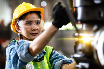 Woman worker wearing safety goggles control lathe machine to drill components. Metal lathe...