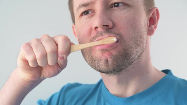 Adult Caucasian man brushes his teeth with a bamboo toothbrush in a light bathroom. no plastic concept.