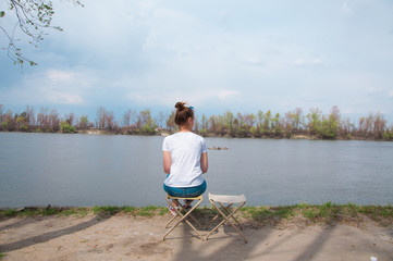 young girl sitting on chair along waiting smb on the river loneliness