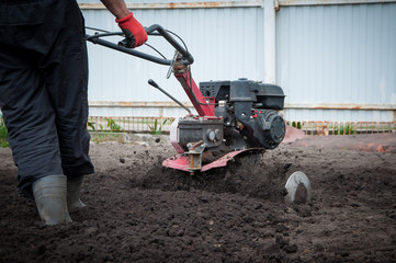 .man works on a cultivator machine in a garden in galoshes in spring