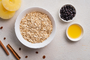 Raw oatmeal with berries, pineapple, honey on a white background. Cooking a healthy breakfast. Top view.