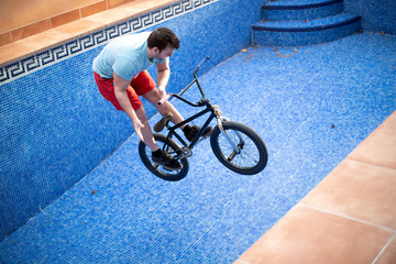 Young man on a small black bmx bike inside a swimming pool with blue background
