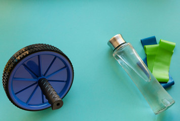 gymnastic wheel for press. 
bottle of water and fitness elastic band on blue background.Sport trend. Fitness concept
