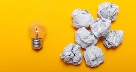 Inspiration concept crumpled paper and light bulb metaphor for good idea. White crumpled paper and light bulb on yellow background, flat lay.