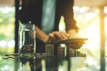 Closeup image of a businesswoman calculating with coins stack and a glass money jar for saving and financial concept