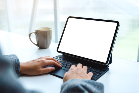 Mockup image of hands using and typing on tablet keyboard with blank white desktop screen as computer pc , coffee cup on the table