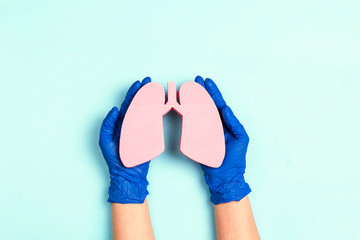 Hands in medical gloves protect human lungs on blue background.