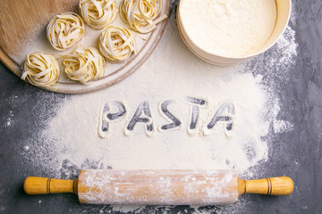 Homemade uncooked pasta tagliatelle and rocking for the dough on black background. Making fresh...