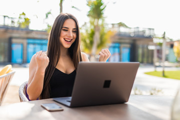 Excited smiling woman celebrating online win, using laptop in cafe, looking at screen, screaming with raising hands, receiving email with good news, new opportunity, great exam or test results