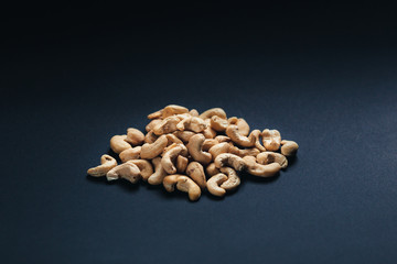 On a dark background, peeled cashew nuts are scattered. Hazelnuts poured on a black background