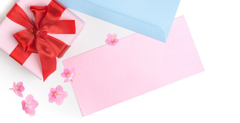 Pink gift box with red bow and blank greeting card for Valentine's day, love letter or wedding invitation. Top view. White background decorated with pink flowers.