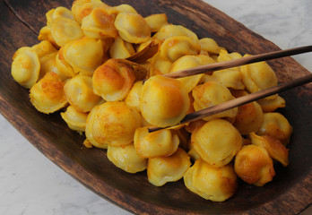 
fried ravioli in olive oil and served in a wooden plate on a marble table.