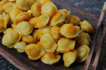 
fried ravioli in olive oil and served in a wooden plate on a marble table.