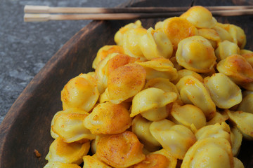 
fried ravioli in olive oil and served in a wooden plate on a marble table.