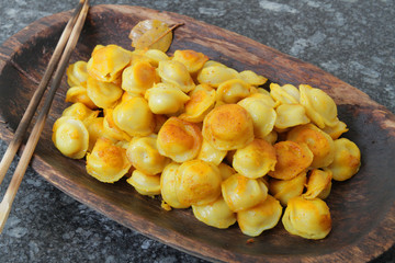 
fried ravioli in olive oil and served in a wooden plate on a marble table.