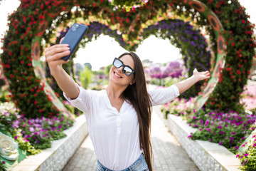 Young pretty woman tourist take selfie on the phone in miracle garden with colorfull frowers hearts