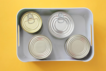 Donation. Food donations on a yellow background. Closed canned beef, pork, corn, green peas in a box. The view.