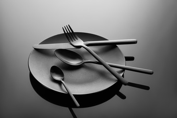 black plate, spoon, tea spoon, knife, fork on black gradient table background
