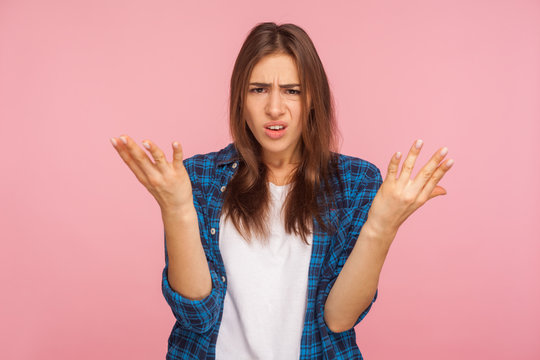 What do you want? Portrait of annoyed girl in checkered shirt raising arms in questioning gesture, saying I don't understand problem, looking indignant. indoor studio shot isolated on pink background