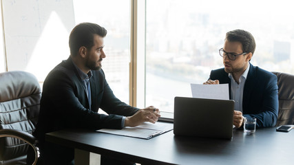 Business partners discussing negotiating contract conditions sitting at table in modern office,...