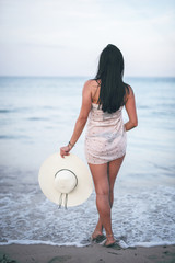Beautiful dark haired young woman standing on the Mallorca becah holding her nice big hat and watching sea, Enjoying nice view and sunny weather, summer holidays