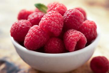 fresh organic raspberries in a white bowl with a bit of mint